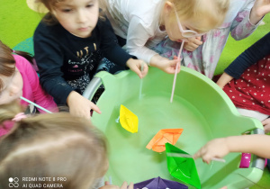 W misce z wodą kolorowe, papierowe łódeczki. Dzieci wprawiają je w ruch dmuchając na nie przez słomki